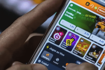 Pessoa usando aplicativo de apostas no smartphone. Tela mostra opções de jogos ao vivo e esportes como futebol e basquete.