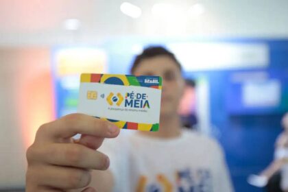 Pessoa segurando um cartão Pé de Meia, iniciativa para poupança estudantil no Brasil, destacando o chip e design colorido.