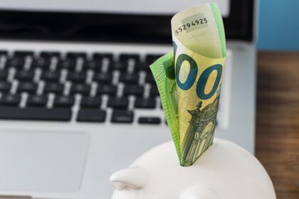 Cofrinho com cédula de euro, gráfico crescente e lupa sobre mesa, simbolizando economia e finanças pessoais.