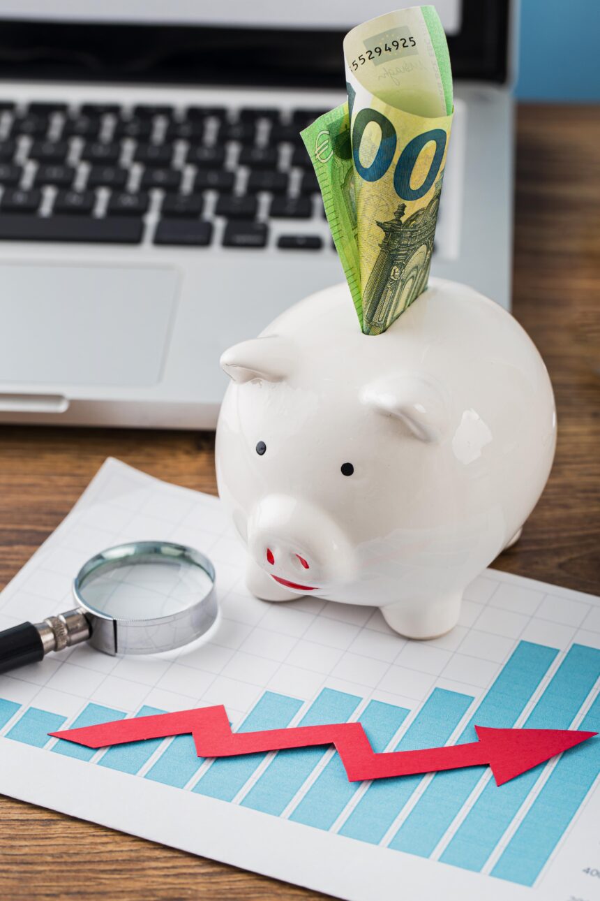 Cofrinho com cédula de euro, gráfico crescente e lupa sobre mesa, simbolizando economia e finanças pessoais.