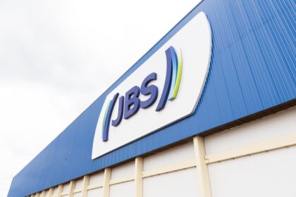 Fachada de prédio industrial da JBS com logotipo em destaque, refletindo estrutura da empresa no setor alimentício.