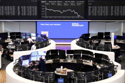 Operadores de bolsa em estações de trabalho na Bolsa de Frankfurt, com múltiplos monitores exibindo dados financeiros em tempo real.