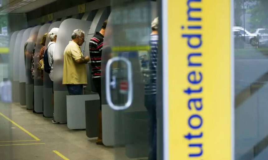 Clientes utilizam caixas eletrônicos em um banco para transações financeiras, destacando o serviço de autoatendimento.