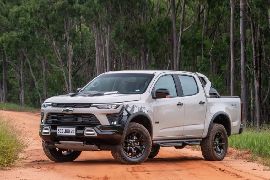 Caminhonete branca Chevrolet em estrada de terra, cercada por árvores, destacando-se em um cenário de aventura off-road.