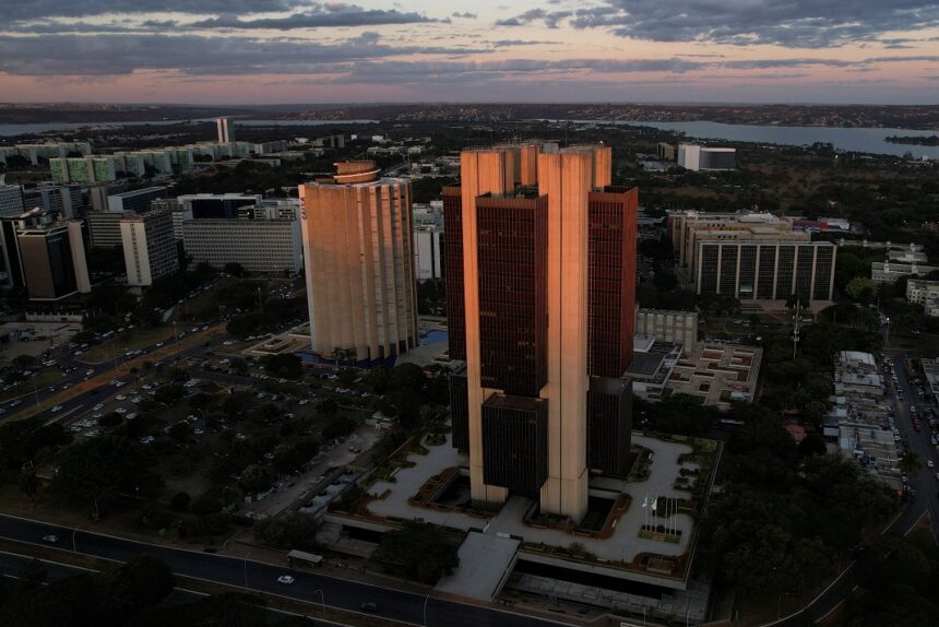 Vista aérea de Brasília ao entardecer, destacando grandes edifícios e vias movimentadas, com o Lago Paranoá ao fundo.