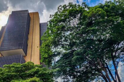 Edifício alto com fachada moderna em contraste com copas de árvores exuberantes, ressaltando urbanismo e natureza juntos.