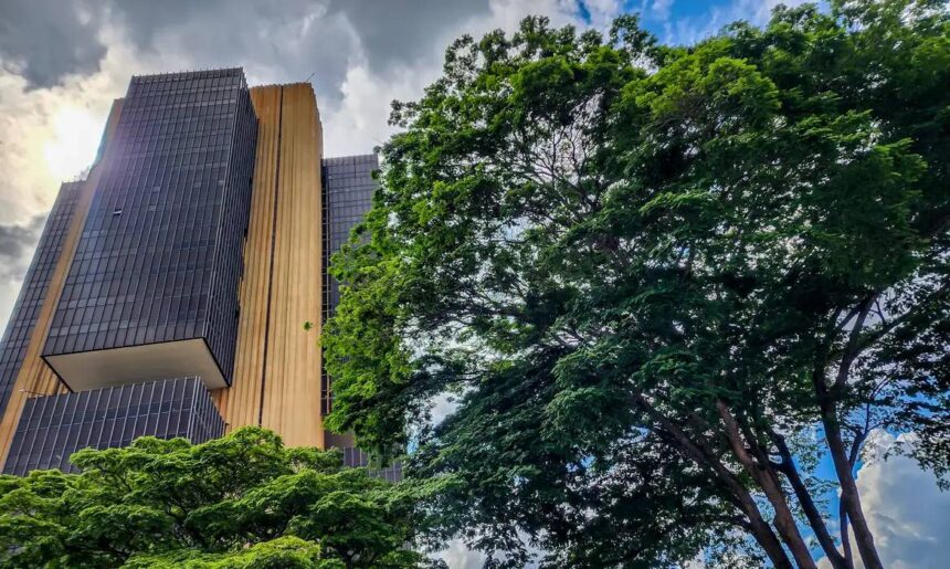 Edifício alto com fachada moderna em contraste com copas de árvores exuberantes, ressaltando urbanismo e natureza juntos.