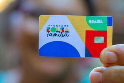 Cartão do Programa Bolsa Família, colorido, sendo segurado por uma mão. Benefício social do governo brasileiro.