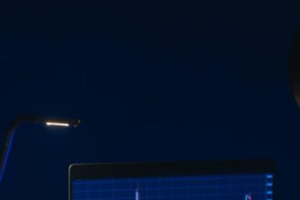 Pessoa analisando gráficos de ações em laptop sob baixa iluminação, destacando tendências do mercado financeiro.