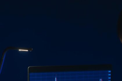 Pessoa analisando gráficos de ações em laptop sob baixa iluminação, destacando tendências do mercado financeiro.