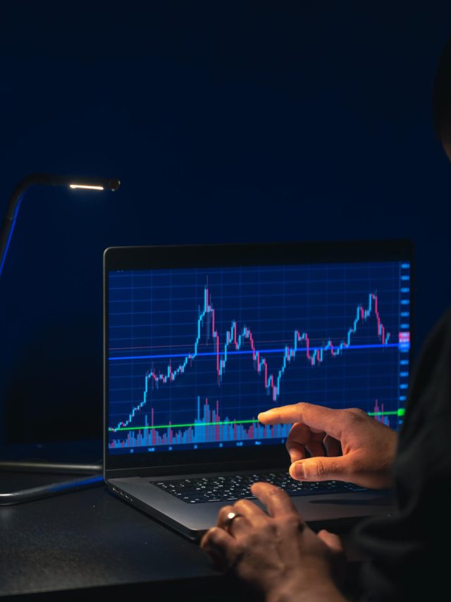 Pessoa analisando gráficos de ações em laptop sob baixa iluminação, destacando tendências do mercado financeiro.