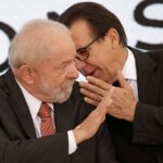 Dois homens em trajes formais interagem em uma conversa privada, conferindo um tom de confidencialidade ao momento.