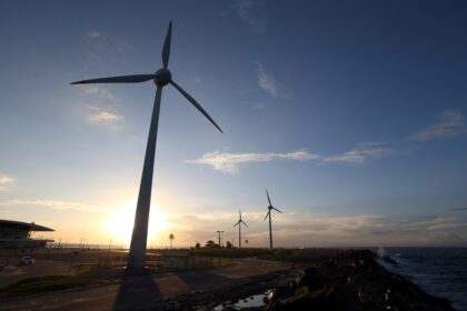 Turbinas eólicas em um parque à beira-mar ao entardecer, aproveitando a energia renovável com o sol ao fundo.