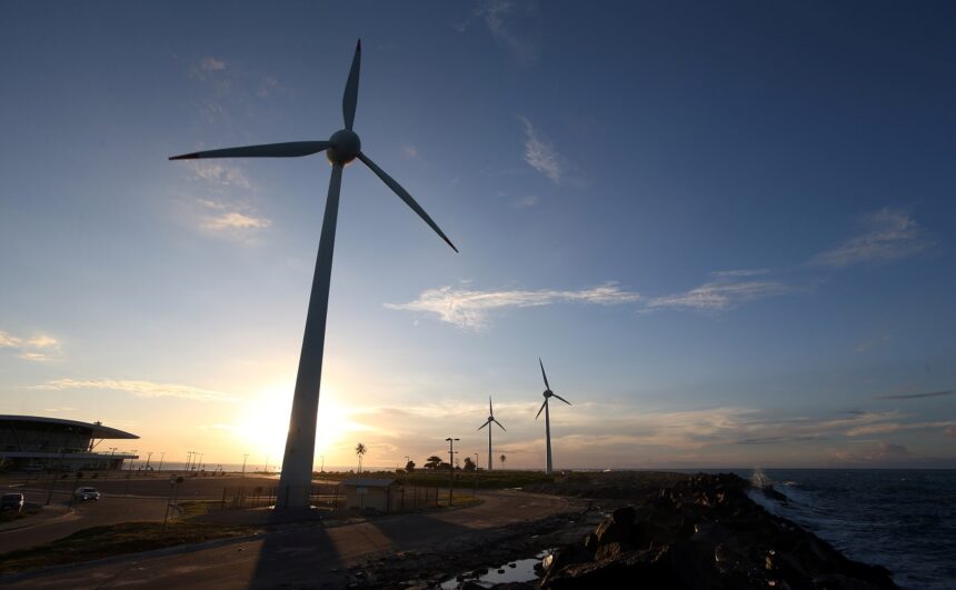Turbinas eólicas em um parque à beira-mar ao entardecer, aproveitando a energia renovável com o sol ao fundo.