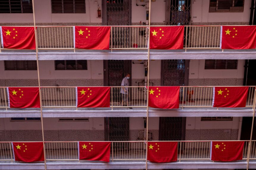 Corredor de edifício com bandeiras da China penduradas, mostrando patriotismo. Pessoa passando ao fundo, usando máscara.