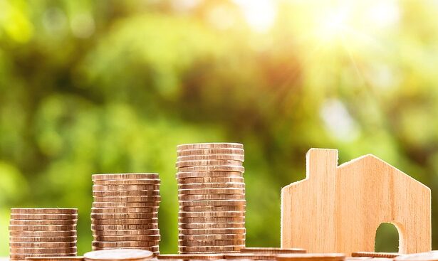Moedas empilhadas ao lado de uma casa em miniatura, simbolizando o conceito de economia doméstica e investimento em imóveis.