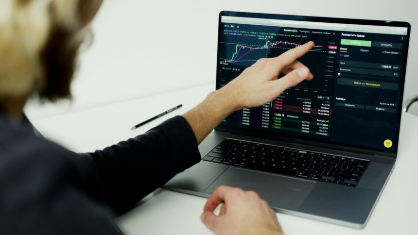 Pessoa analisando gráficos e dados de trading em laptop, com foco na estratégia de investimento e mercado financeiro.