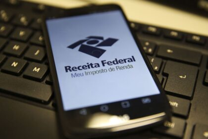 Celular sobre teclado exibe app da Receita Federal para declaração de Imposto de Renda, destacando tecnologia e finanças.