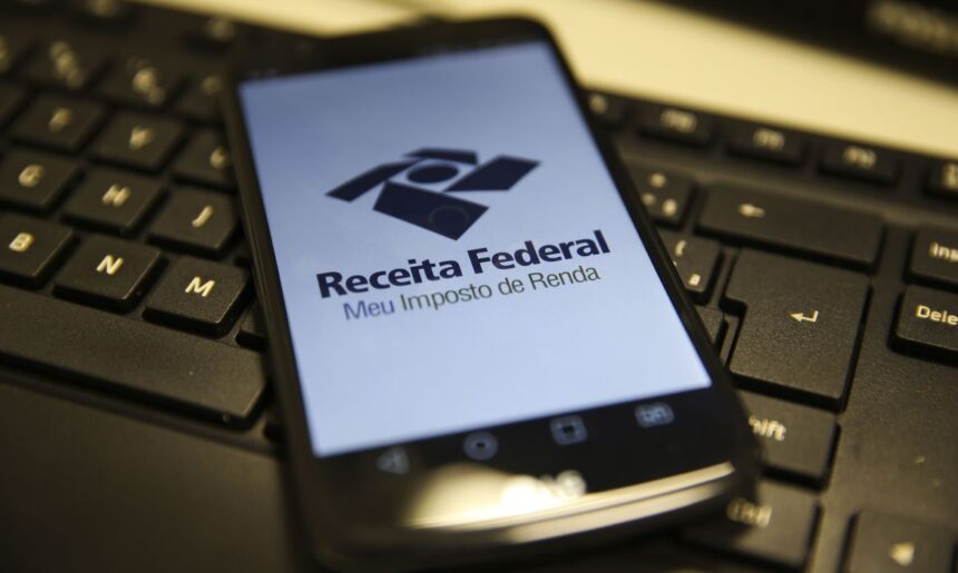 Celular sobre teclado exibe app da Receita Federal para declaração de Imposto de Renda, destacando tecnologia e finanças.