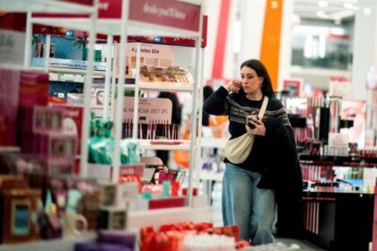 Mulher comprando em loja de cosméticos, examinando produtos de beleza nas prateleiras, ambiente iluminado e organizado.