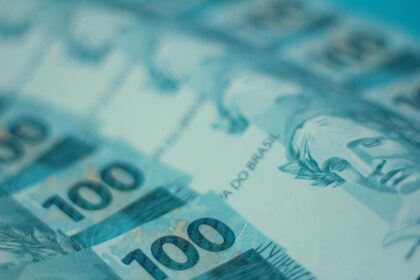 Notas de 100 reais do Brasil enfileiradas, destacando o rosto da efígie e detalhes em azul e verde.