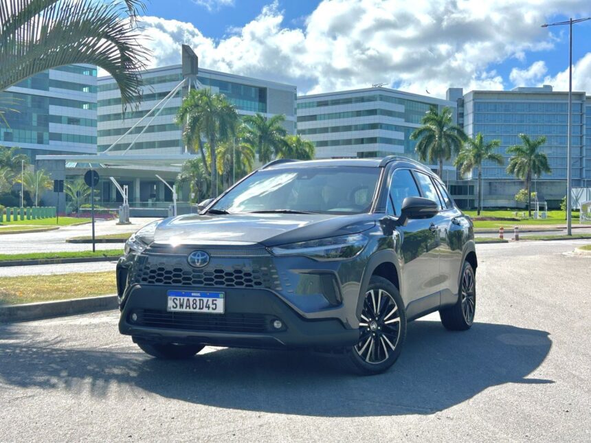 SUV Toyota moderno estacionado em frente a prédio empresarial com palmeiras, céu azul e nuvens ao fundo.