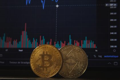 Moedas de Bitcoin e Ethereum em frente a gráfico de ações em tela, ilustrando o mercado de criptomoedas e suas flutuações.