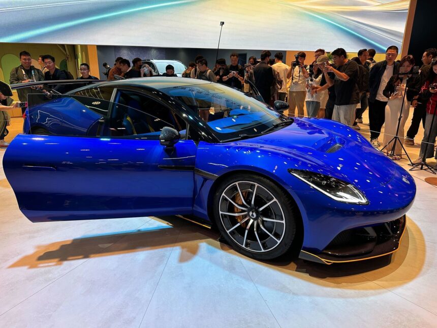 Carro esportivo azul em exibição, com porta aberta, cercado por pessoas tirando fotos em um salão de automóveis.
