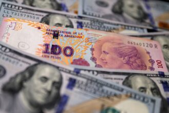 Cédula de 100 pesos argentinos sobre notas de 100 dólares, destacando contraste entre moedas argentina e americana.