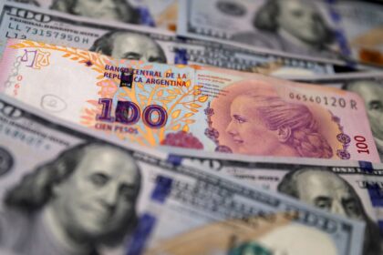 Cédula de 100 pesos argentinos sobre notas de 100 dólares, destacando contraste entre moedas argentina e americana.