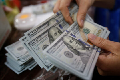Mãos contando notas de cem dólares em um ambiente de escritório, simbolizando finanças e economia.