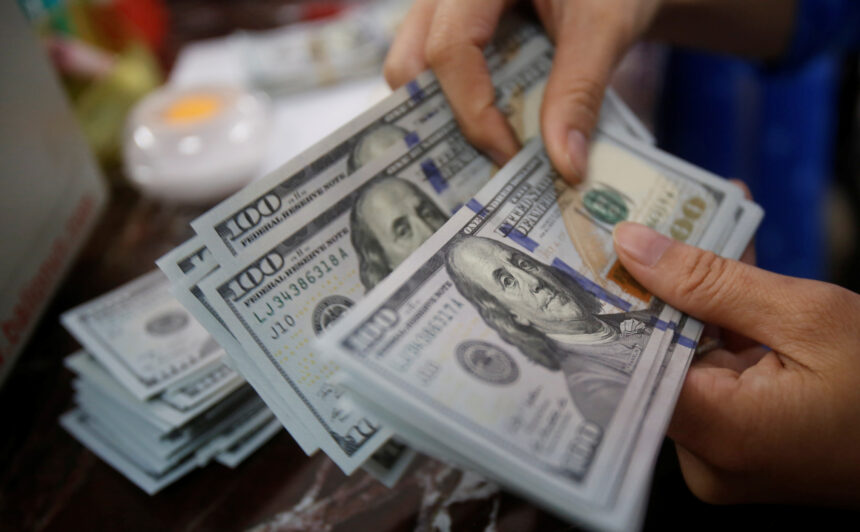 Mãos contando notas de cem dólares em um ambiente de escritório, simbolizando finanças e economia.