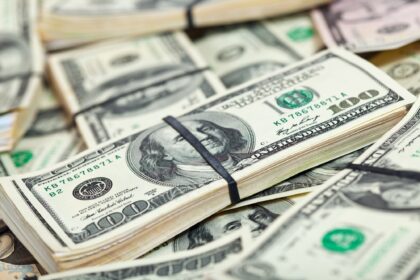 Notas de cem dólares empilhadas e amarradas com elástico, destacando dinheiro em espécie e finanças pessoais.