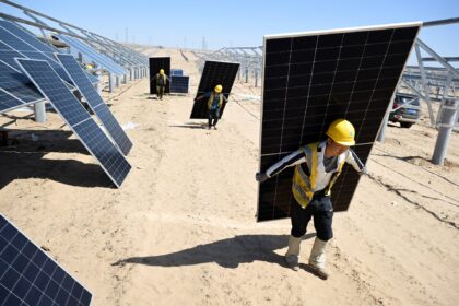 Trabalhadores em um parque solar desértico carregam painéis solares, destacando energias renováveis e tecnologia sustentável.