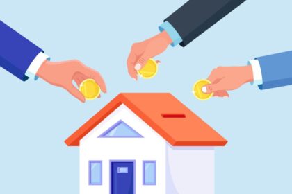 Mãos colocando moedas em miniatura de casa, simbolizando investimento coletivo ou poupança para aquisição imobiliária.