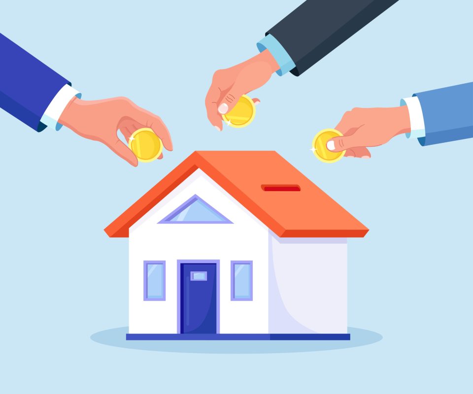 Mãos colocando moedas em miniatura de casa, simbolizando investimento coletivo ou poupança para aquisição imobiliária.