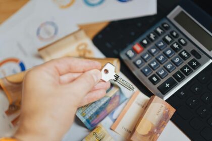 Mão segura chave ao lado de cédulas de euro e calculadora, simbolizando finanças e investimentos imobiliários.