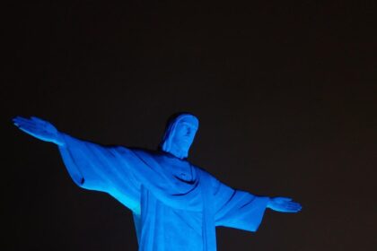 Estátua do Cristo Redentor iluminada de azul à noite, destacando-se contra o céu escuro no Rio de Janeiro.