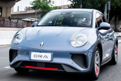 Carro elétrico ORA cinza circula em rua urbana, destacando design moderno e eficiente para mobilidade sustentável.