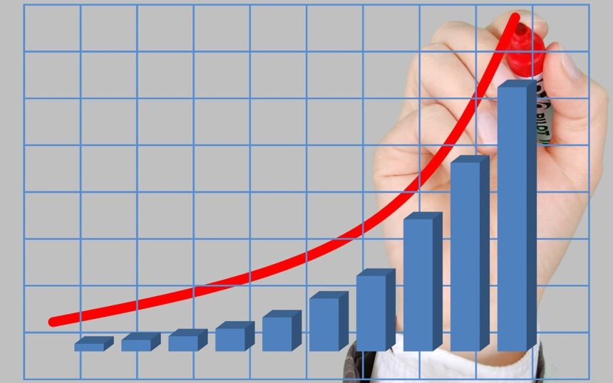 Mão desenha linha de tendência de crescimento em gráfico com barras azuis, destacando sucesso financeiro e progresso.