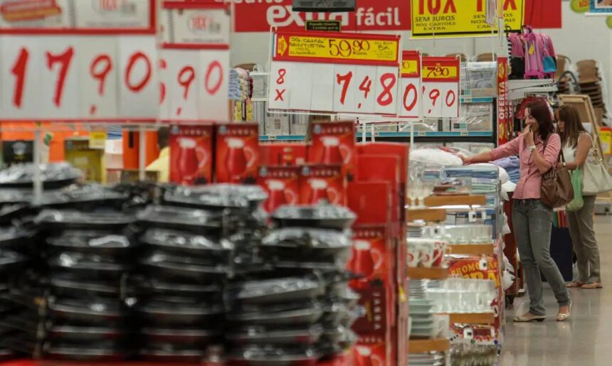Clientes em loja de departamento, cercados por promoções e produtos domésticos, pesquisando preços e escolhendo itens.