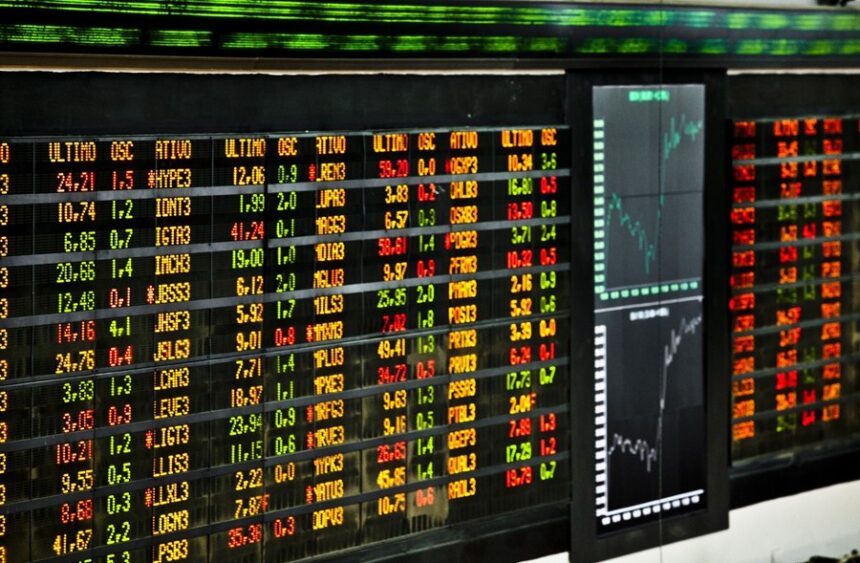 Painel eletrônico de cotações da bolsa de valores, exibindo números em cores variadas, gráficos de tendências ao lado.