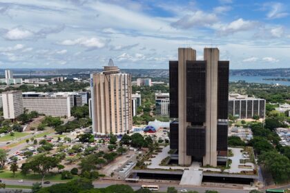Vista aérea de Brasília com prédios do Banco Central e Caixa, cercados por árvores e avenidas movimentadas.