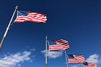 Bandeiras dos Estados Unidos tremulam contra o céu azul, simbolizando patriotismo e orgulho americano.