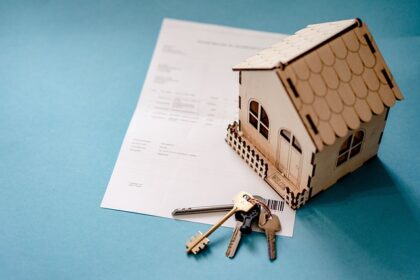 Miniatura de casa em madeira sobre documento de compra de imóvel com chaves ao lado, simbolizando aquisição imobiliária.