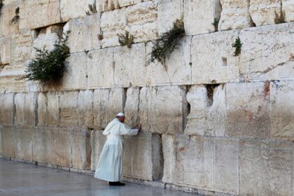 Pessoa em vestes brancas em oração no Muro das Lamentações, Jerusalém, destacando espiritualidade e tradição religiosa.
