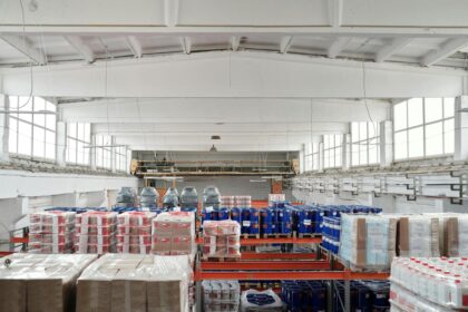 Armazém organizado com diversas prateleiras cheias de mercadorias embaladas, em um ambiente industrial amplo e iluminado.