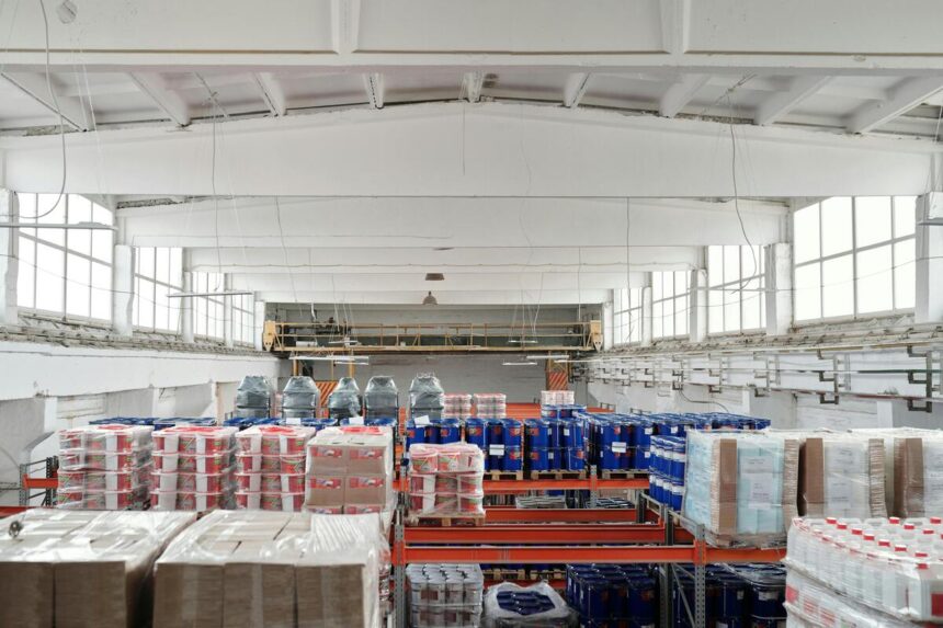 Armazém organizado com diversas prateleiras cheias de mercadorias embaladas, em um ambiente industrial amplo e iluminado.