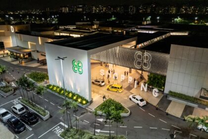 Vista aérea de shopping à noite, com logo iluminado e entrada movimentada por táxis e pedestres, realçando lazer urbano.