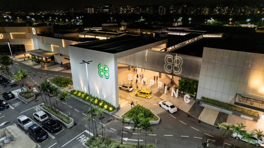Vista aérea de shopping à noite, com logo iluminado e entrada movimentada por táxis e pedestres, realçando lazer urbano.